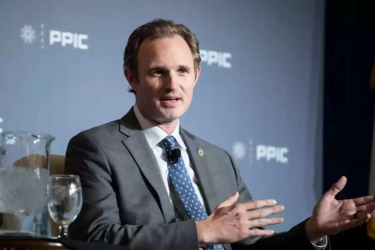 Man in a gray suit speaking and gesturing during an event with a blue background and PPIC logo Man in a gray suit speaking and gesturing during an event with a blue background and PPIC logo