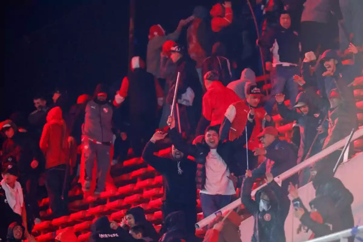 Fans in the stands of a stadium wearing warm clothing, some holding sticks, in a tense and chaotic atmosphere. Fans in the stands of a stadium wearing warm clothing, some holding sticks, in a tense and chaotic atmosphere.