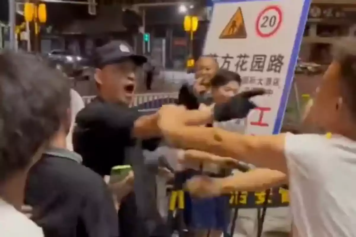 Several people argue and point at each other in the street at night in front of a warning sign. Several people argue and point at each other in the street at night in front of a warning sign.