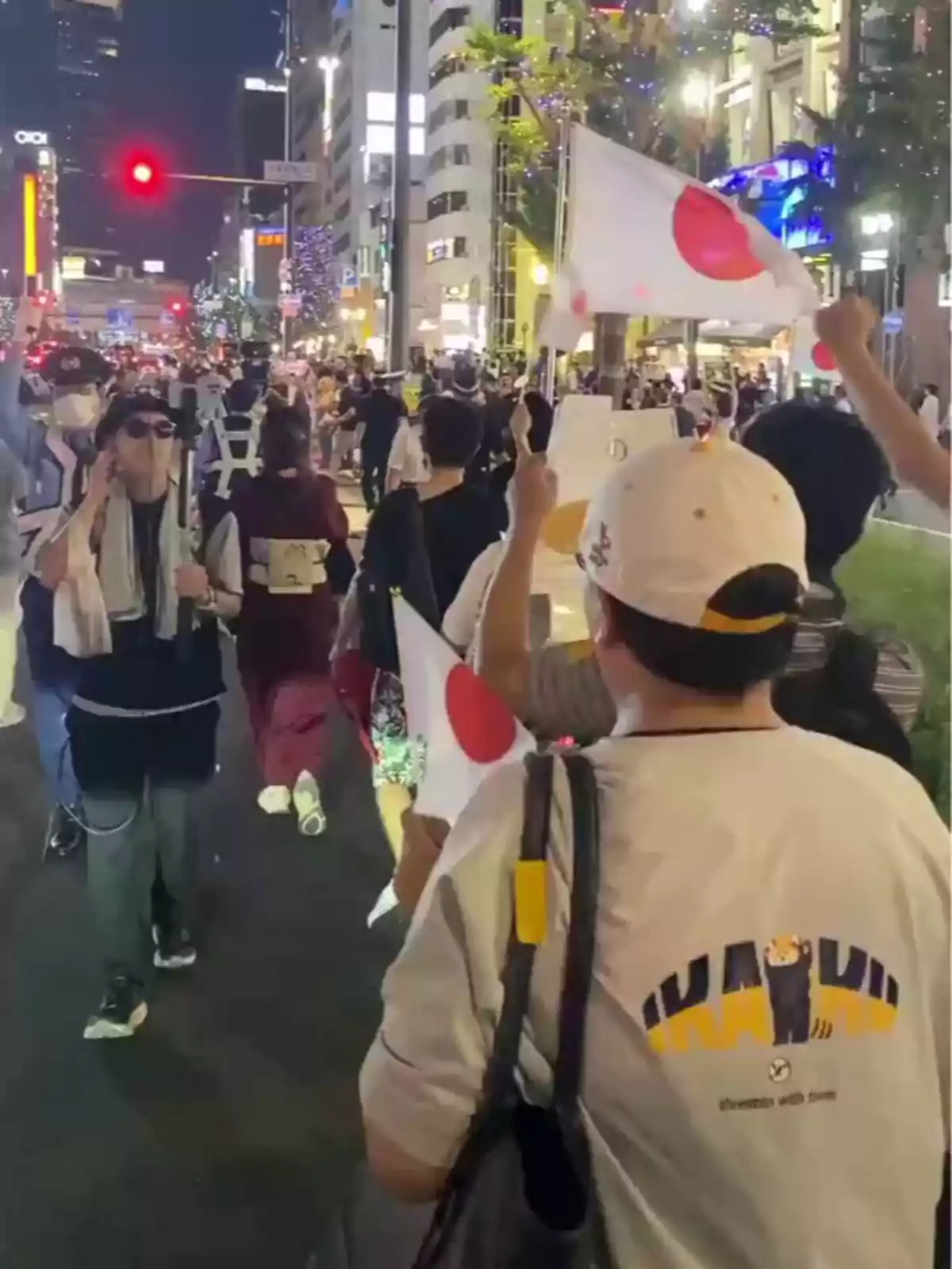 People marching down a brightly lit street at night while waving Japanese flags People marching down a brightly lit street at night while waving Japanese flags