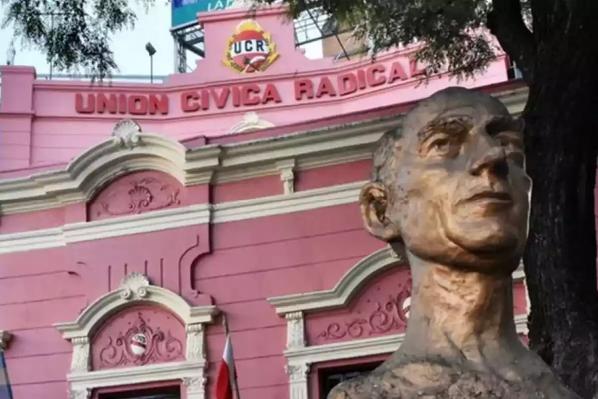 Fachada de un edificio rosa de la Unión Cívica Radical con un busto de bronce en primer plano y un árbol al costado