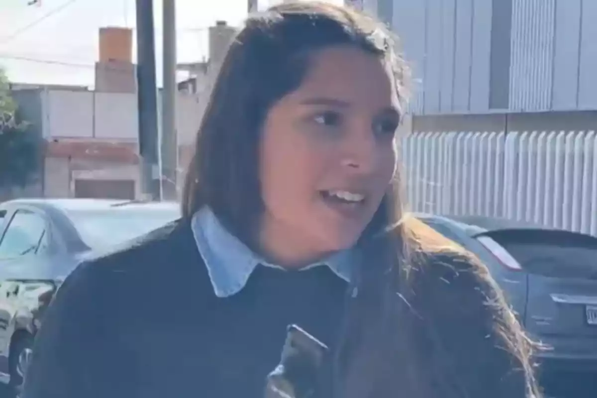 Mujer joven de cabello largo hablando al aire libre con autos y edificios de fondo