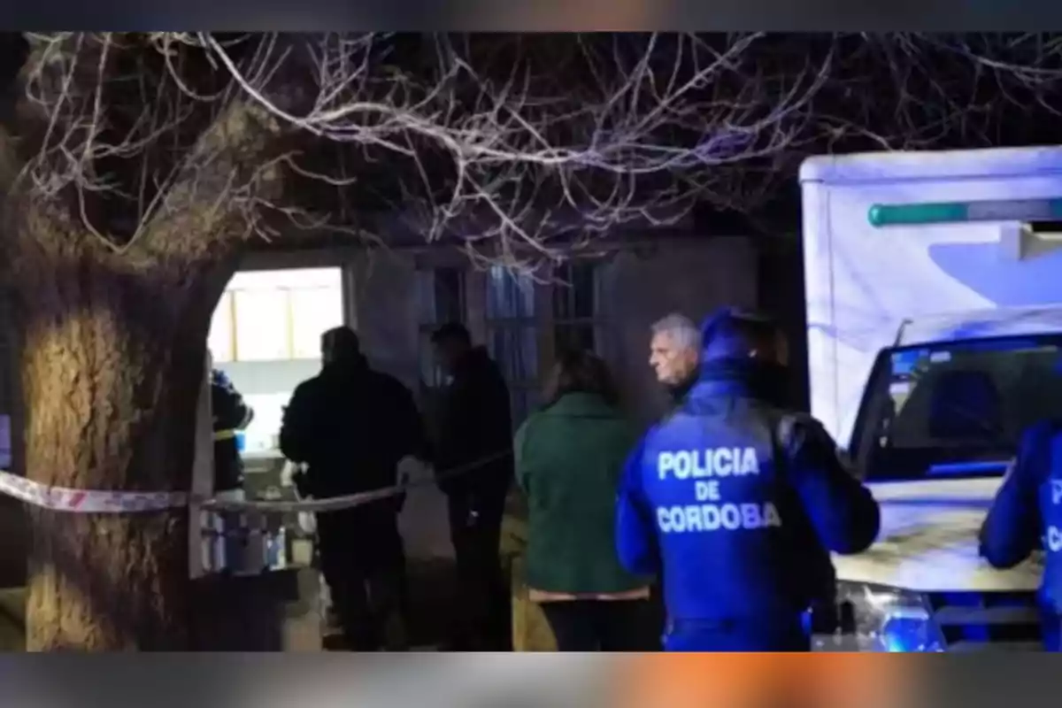 Varios policías y personas se encuentran en la entrada de una casa acordonada por una cinta, junto a un árbol sin hojas y una camioneta blanca, durante la noche. Varios policías y personas se encuentran en la entrada de una casa acordonada por una cinta, junto a un árbol sin hojas y una camioneta blanca, durante la noche.