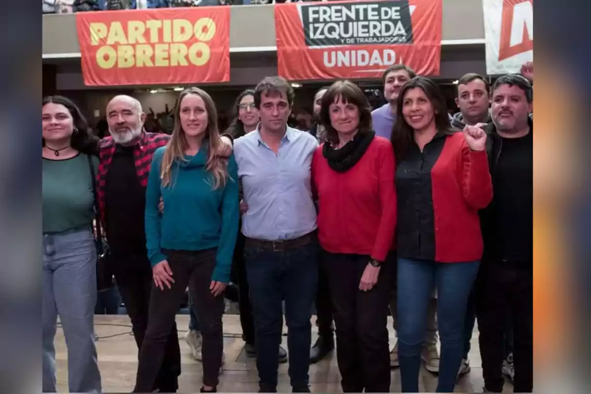 Un grupo de personas posando juntas en un evento político con pancartas de partidos de izquierda al fondo