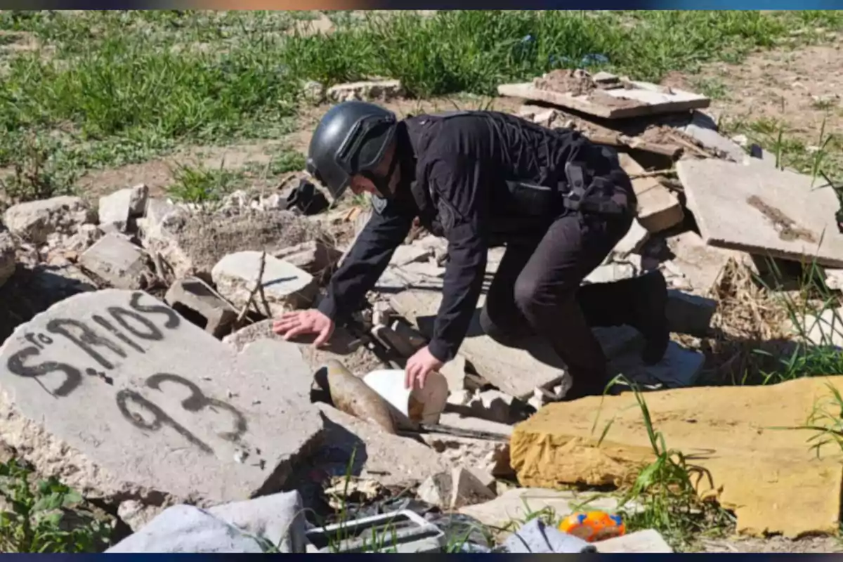 Police officer wearing a helmet inspecting rubble and concrete on a grassy area with scattered objects