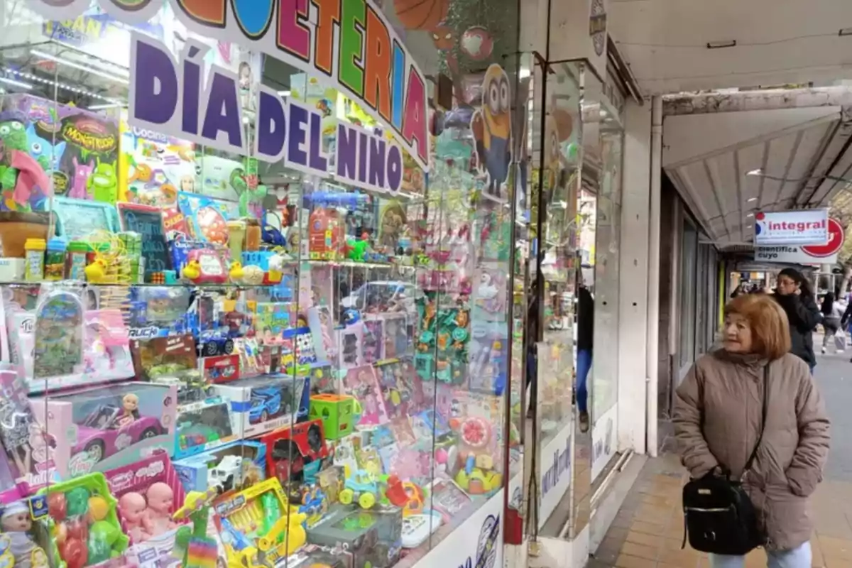 Una mujer observa el escaparate de una juguetería llena de juguetes coloridos y decoraciones por el Día del Niño en una calle comercial