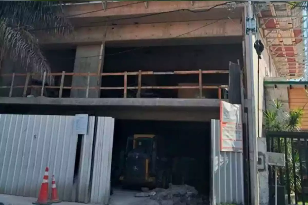 Edificio en construcción con una entrada cercada por láminas metálicas y dos conos naranjas frente a la entrada