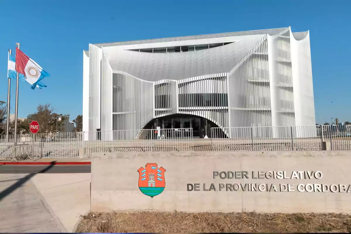 Modern building of the Legislative Power of the Province of Córdoba with Argentine flags waving and a stop sign at the entrance