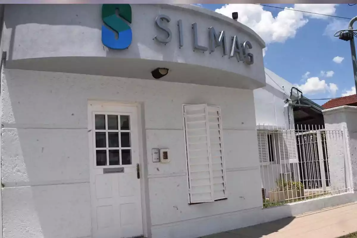 Facade of a white building with a sign that says SILMAG and an entrance door next to a window with bars