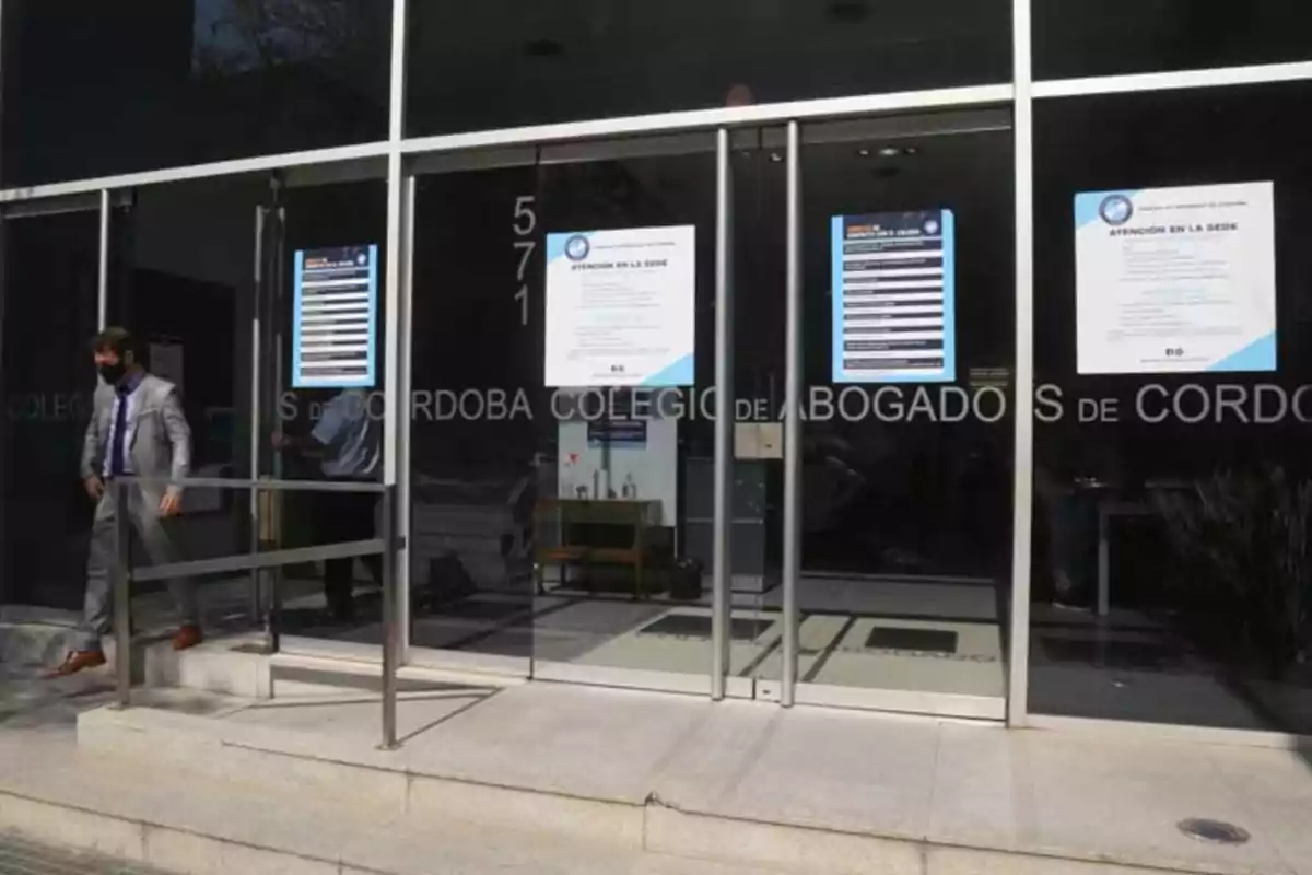 Facade of a glass building with informational signs on the doors and a man in a suit and face mask exiting the place