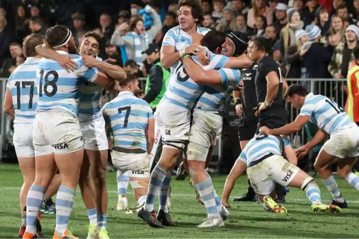 Rugby players in light blue and white uniforms celebrate enthusiastically on the field after a match while the crowd watches from the stands. Rugby players in light blue and white uniforms celebrate enthusiastically on the field after a match while the crowd watches from the stands.