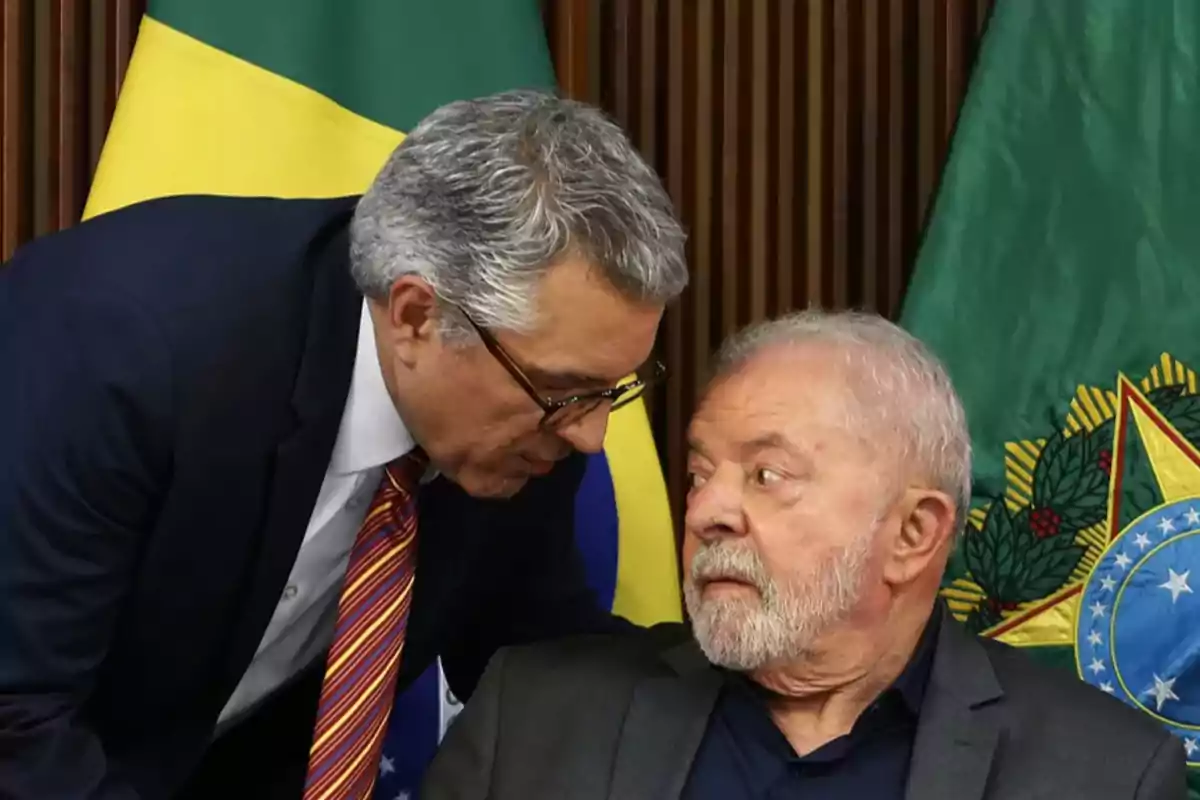 Dos hombres conversan en primer plano con banderas de Brasil al fondo