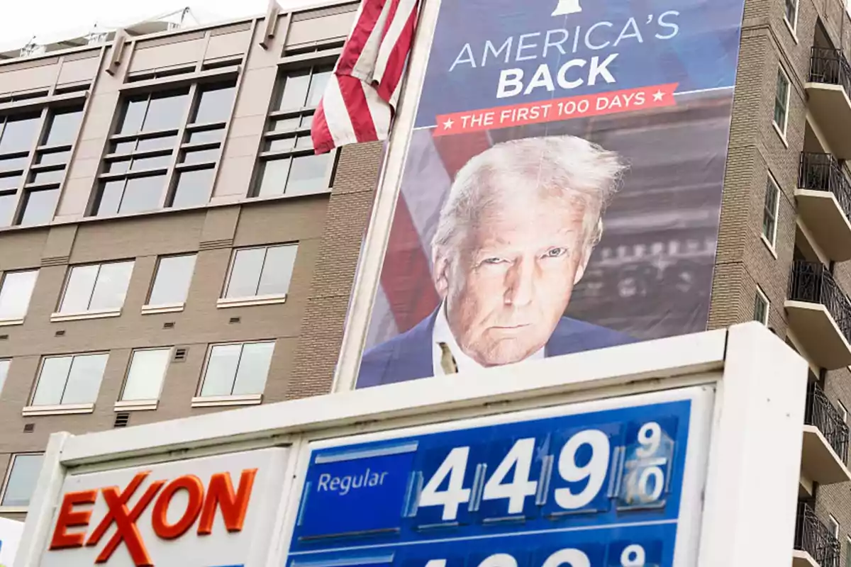Cartel con la imagen de un hombre de cabello rubio y expresión seria junto a una bandera de Estados Unidos sobre un edificio, con un letrero de gasolinera Exxon mostrando el precio de la gasolina en primer plano