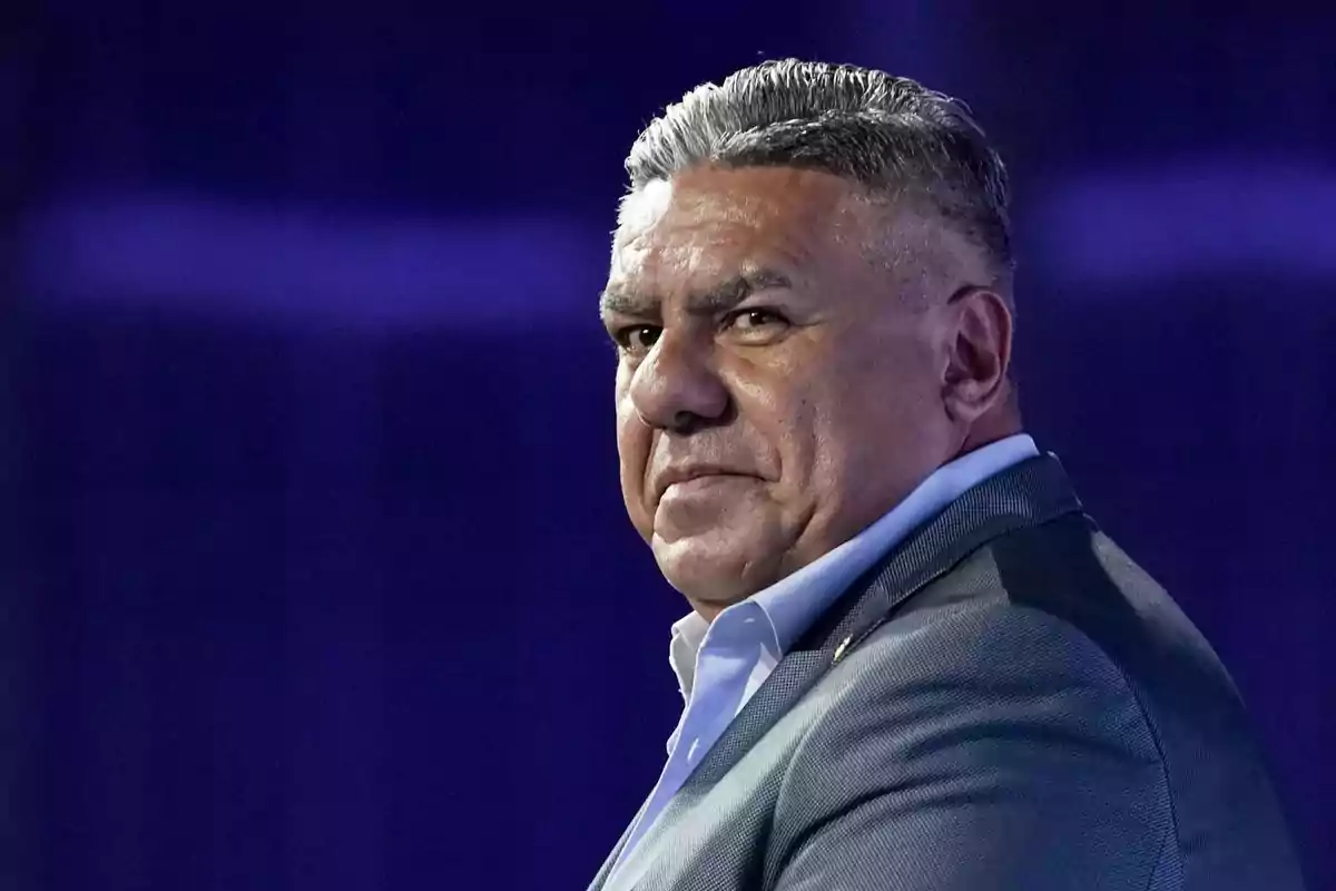 Gray-haired, short-haired man in a dark suit looking at the camera against a blurred blue background Gray-haired, short-haired man in a dark suit looking at the camera against a blurred blue background