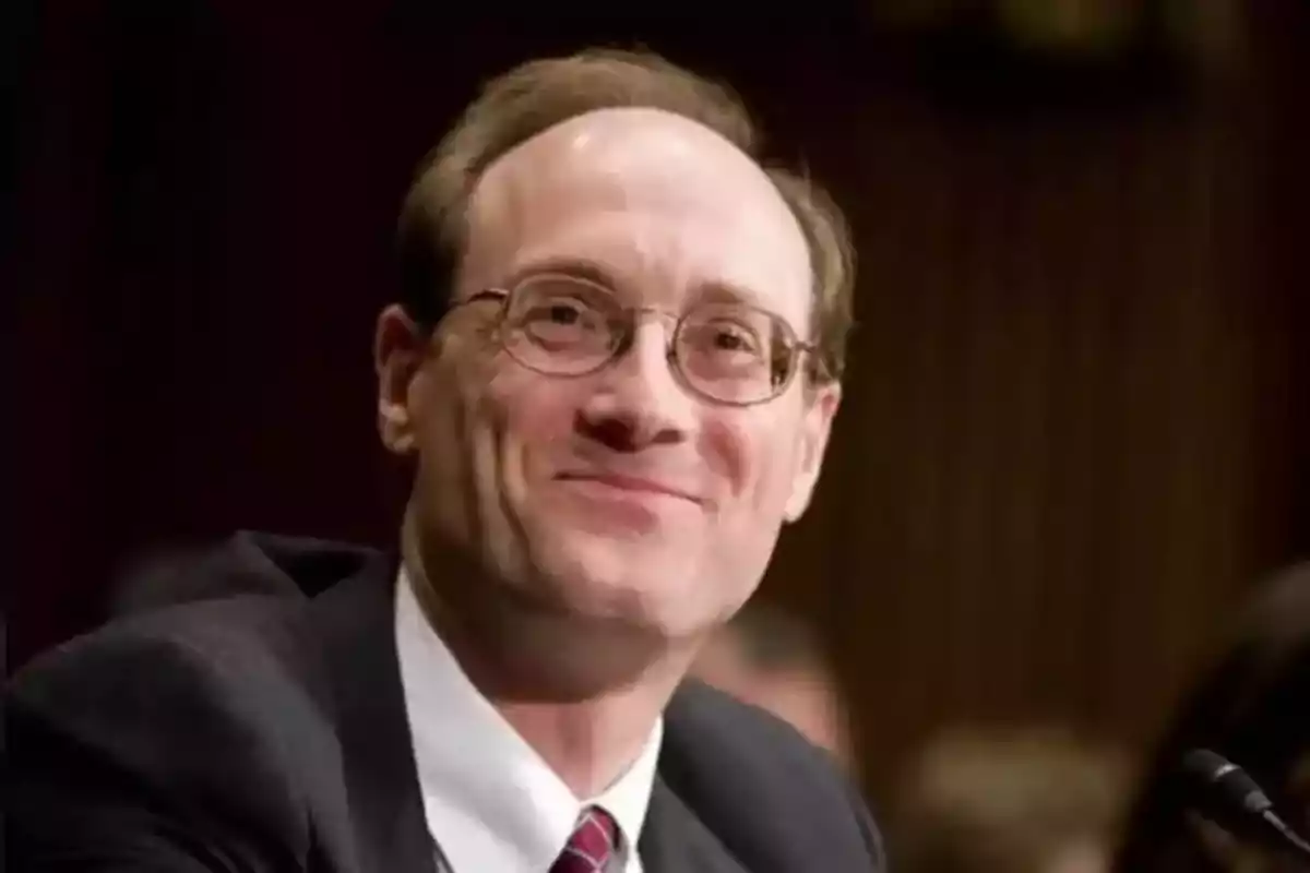 Hombre de mediana edad con gafas y traje sonriendo en un entorno formal