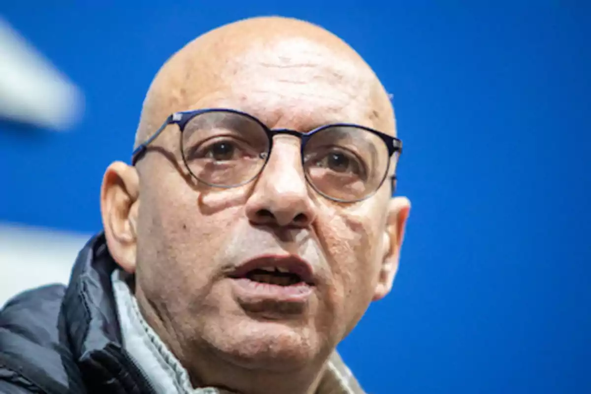 Hombre calvo con gafas y chaqueta oscura frente a un fondo azul Hombre calvo con gafas y chaqueta oscura frente a un fondo azul