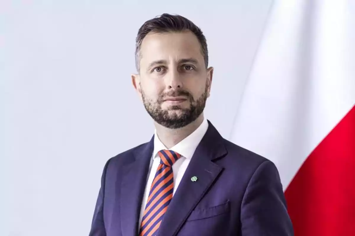 Short-bearded man in a blue suit and orange-and-blue striped tie posing in front of a white and red flag Short-bearded man in a blue suit and orange-and-blue striped tie posing in front of a white and red flag
