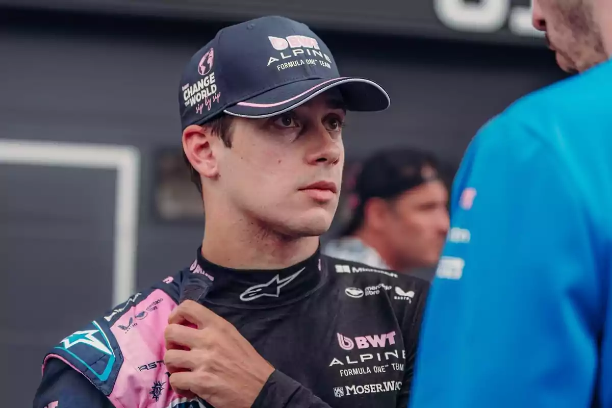 Motorsport driver wearing an Alpine team cap and uniform talking with another person in the paddock