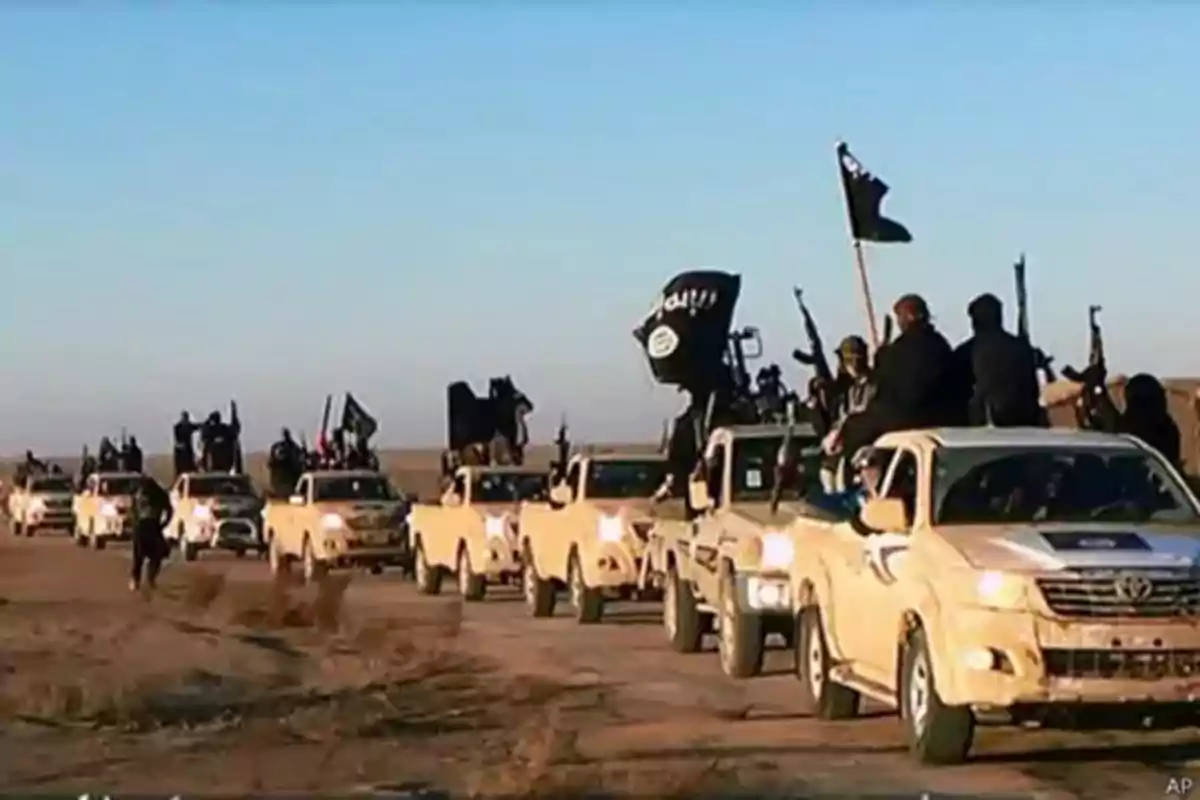 Caravan of beige pickup trucks with armed people and black flags moving along a road in a desert landscape Caravan of beige pickup trucks with armed people and black flags moving along a road in a desert landscape