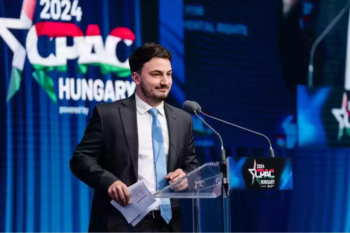 Hombre con traje y corbata azul hablando en un podio durante un evento de CPAC 2024 en Hungría Hombre con traje y corbata azul hablando en un podio durante un evento de CPAC 2024 en Hungría