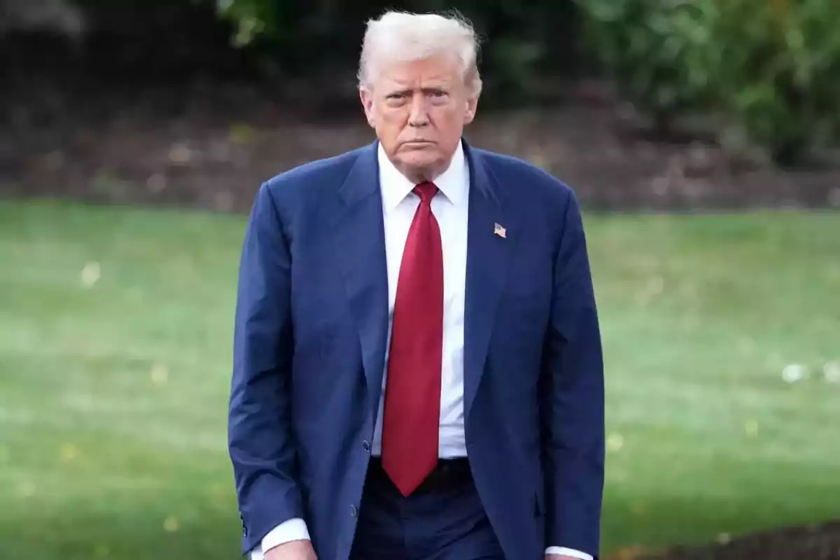 Hombre de cabello rubio con traje azul y corbata roja caminando en un jardín Hombre de cabello rubio con traje azul y corbata roja caminando en un jardín