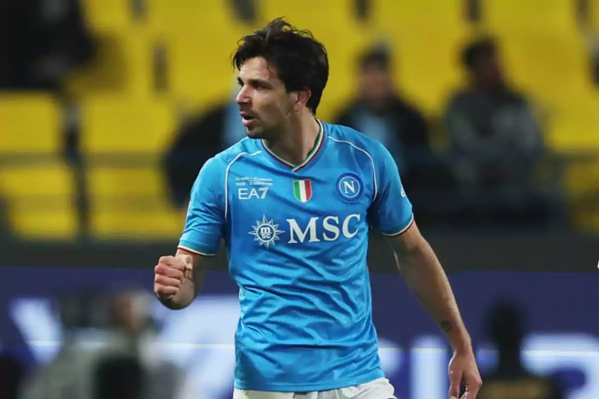 Futbolista del Napoli celebrando en el campo con uniforme azul y fondo de gradas amarillas desenfocadas Futbolista del Napoli celebrando en el campo con uniforme azul y fondo de gradas amarillas desenfocadas