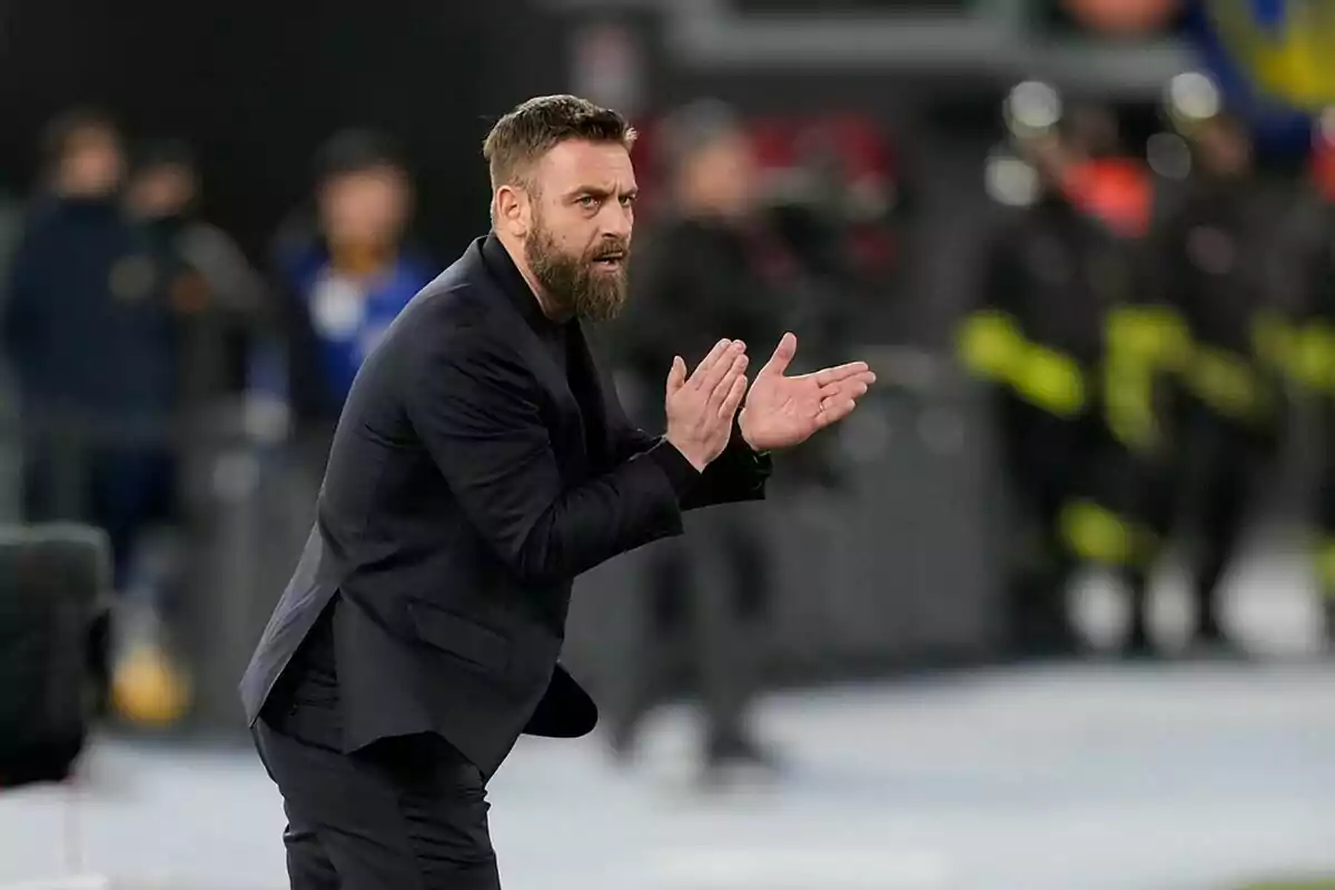 Hombre con barba y traje oscuro aplaudiendo en una cancha de fútbol durante un partido Hombre con barba y traje oscuro aplaudiendo en una cancha de fútbol durante un partido