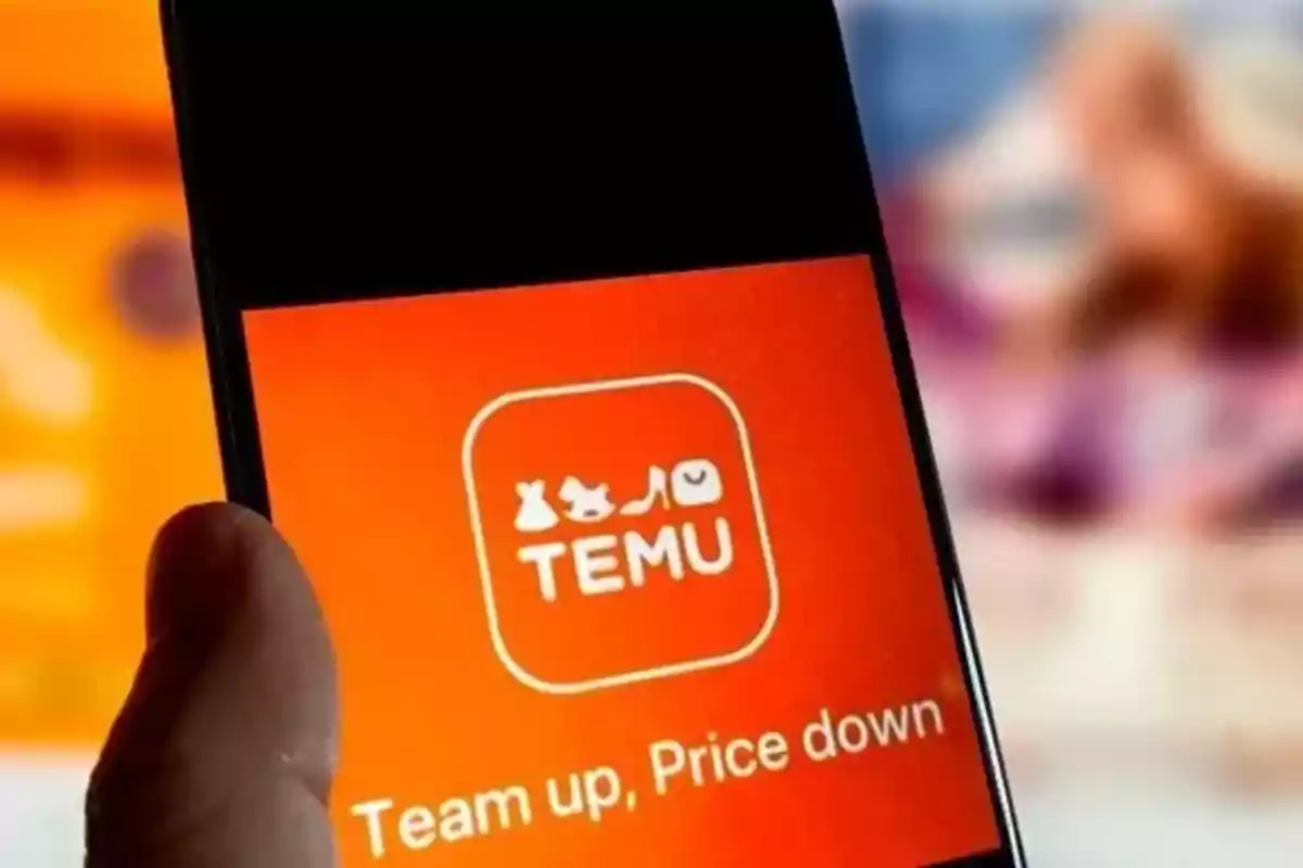 Person holding a mobile phone displaying the Temu app home screen with an orange background and the slogan Person holding a mobile phone displaying the Temu app home screen with an orange background and the slogan