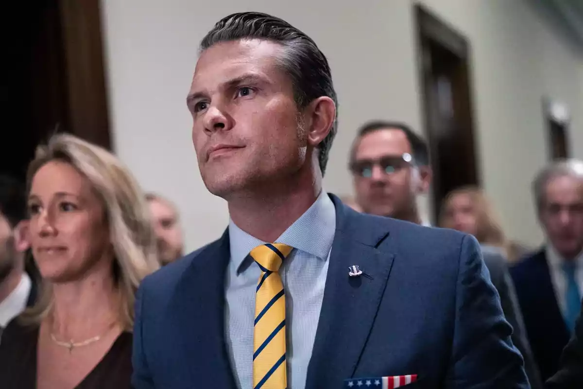 Short-haired man with slicked-back hair wearing a blue suit and a yellow tie with black stripes walking down a hallway accompanied by other people Short-haired man with slicked-back hair wearing a blue suit and a yellow tie with black stripes walking down a hallway accompanied by other people