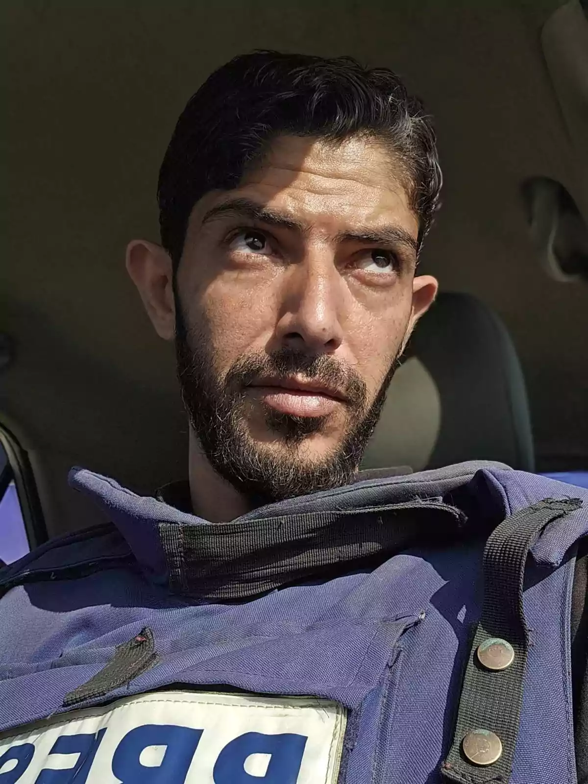 Man wearing a press vest sitting inside a vehicle looking up with a serious expression Man wearing a press vest sitting inside a vehicle looking up with a serious expression