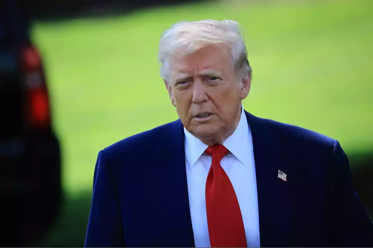 Hombre de cabello rubio con traje azul y corbata roja en un entorno al aire libre con césped verde de fondo Hombre de cabello rubio con traje azul y corbata roja en un entorno al aire libre con césped verde de fondo