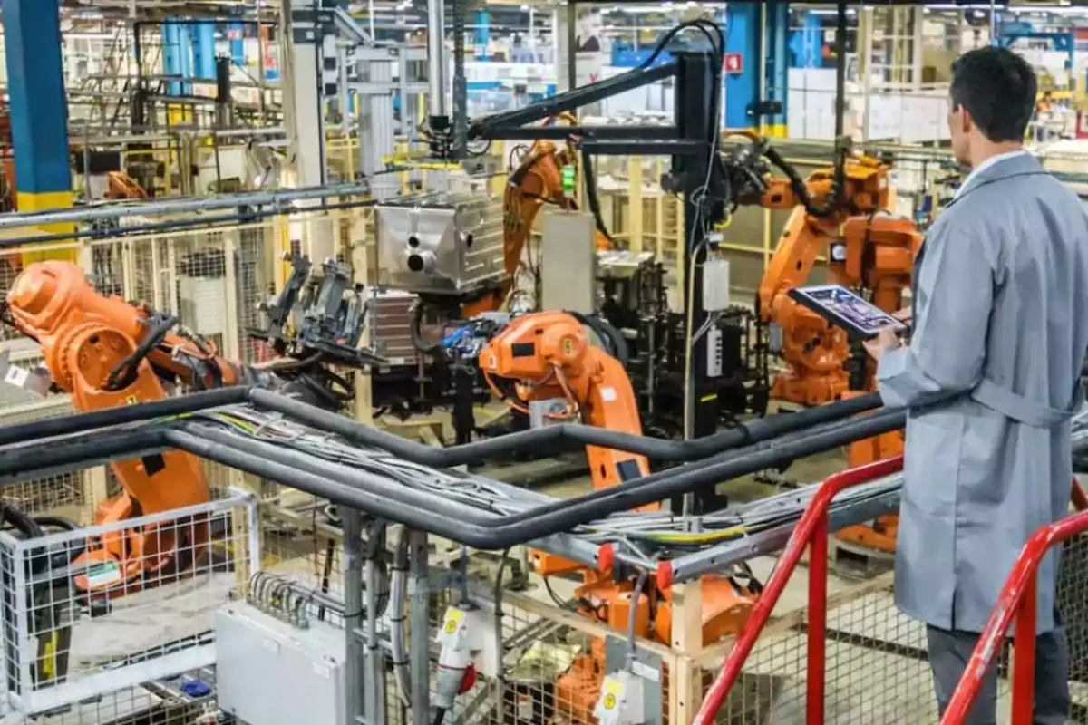 Un ingeniero supervisa robots industriales naranjas trabajando en una línea de producción automatizada dentro de una fábrica moderna