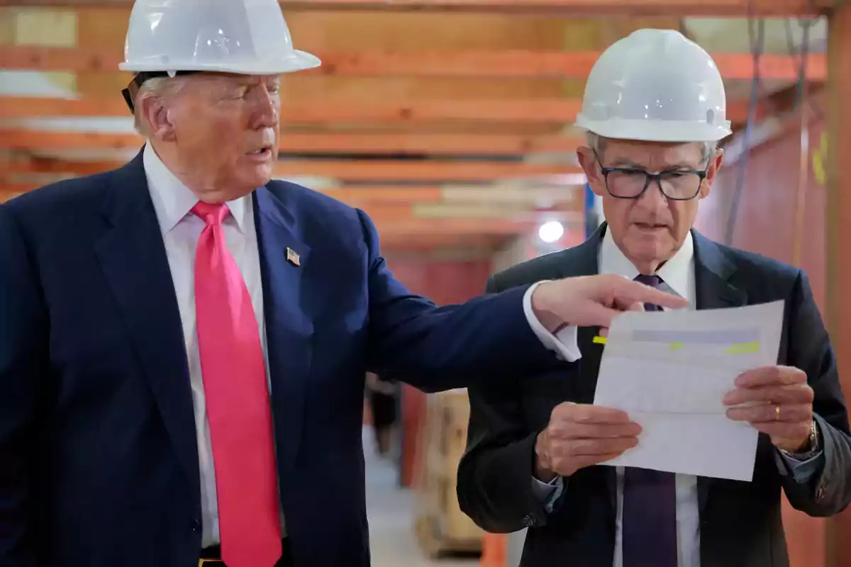 Two men wearing safety helmets and suits review documents at a construction site.