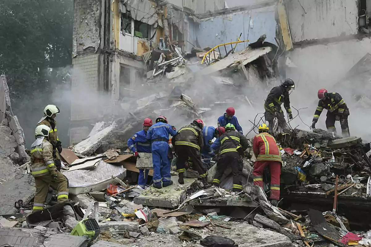 Rescatistas y bomberos trabajan entre los escombros de un edificio derrumbado cubierto de polvo y humo