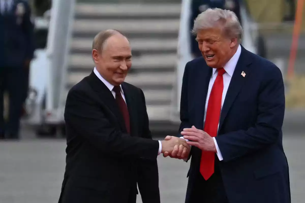 Two men in dark suits shake hands and smile in an outdoor setting with stairs in the background. Two men in dark suits shake hands and smile in an outdoor setting with stairs in the background.
