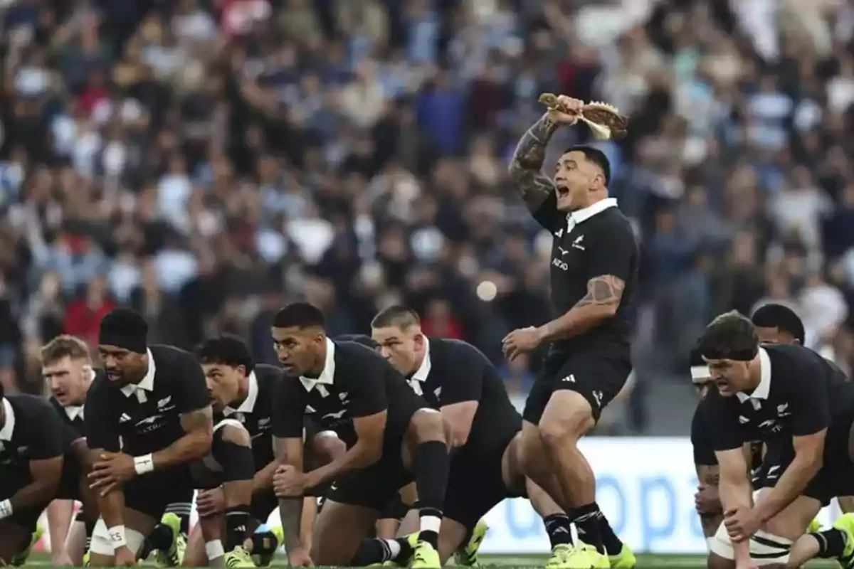 Jugadores de rugby vestidos de negro realizan la tradicional danza haka en el campo antes de un partido frente a una multitud Jugadores de rugby vestidos de negro realizan la tradicional danza haka en el campo antes de un partido frente a una multitud