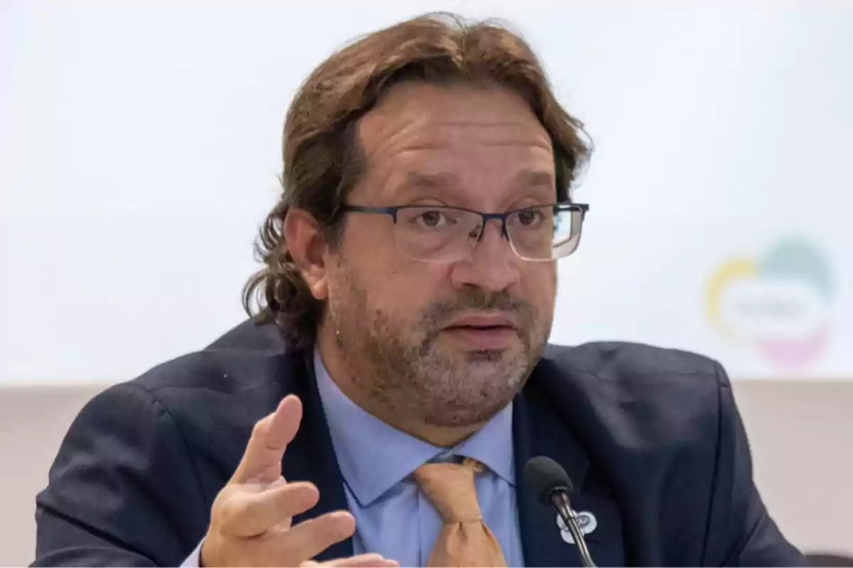 Hombre con gafas y barba hablando frente a un micrófono durante una conferencia Hombre con gafas y barba hablando frente a un micrófono durante una conferencia