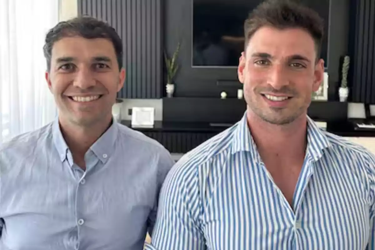 Dos hombres sonrientes posan juntos en una habitación moderna con paredes oscuras y plantas decorativas al fondo Dos hombres sonrientes posan juntos en una habitación moderna con paredes oscuras y plantas decorativas al fondo