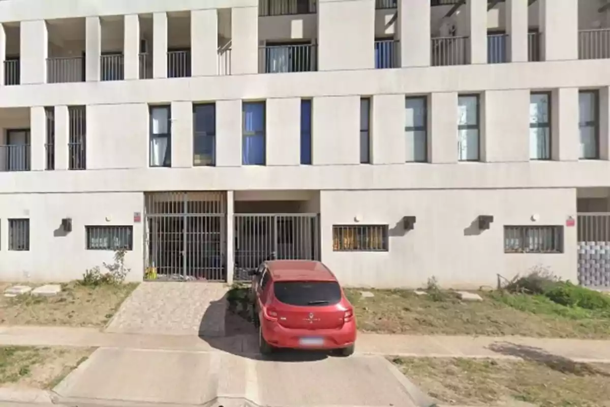 Auto rojo estacionado frente a la entrada de un edificio moderno de varios pisos con ventanas y balcones Auto rojo estacionado frente a la entrada de un edificio moderno de varios pisos con ventanas y balcones