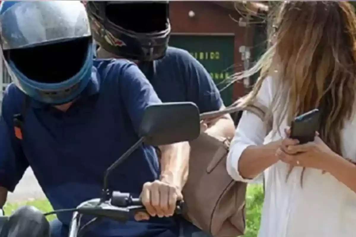 Dos personas en motocicleta le arrebatan el bolso a una mujer que sostiene un teléfono móvil Dos personas en motocicleta le arrebatan el bolso a una mujer que sostiene un teléfono móvil