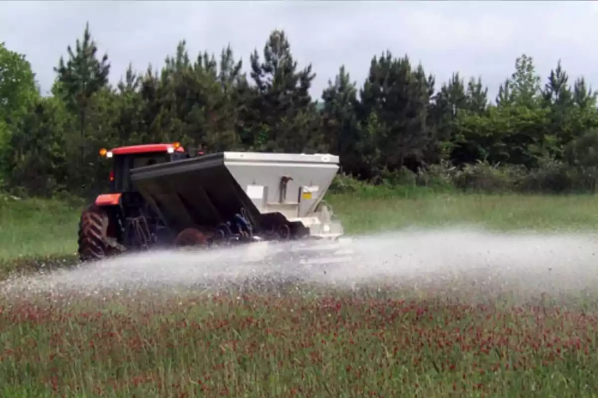 Tractor spreading fertilizer in a green field surrounded by trees Tractor spreading fertilizer in a green field surrounded by trees