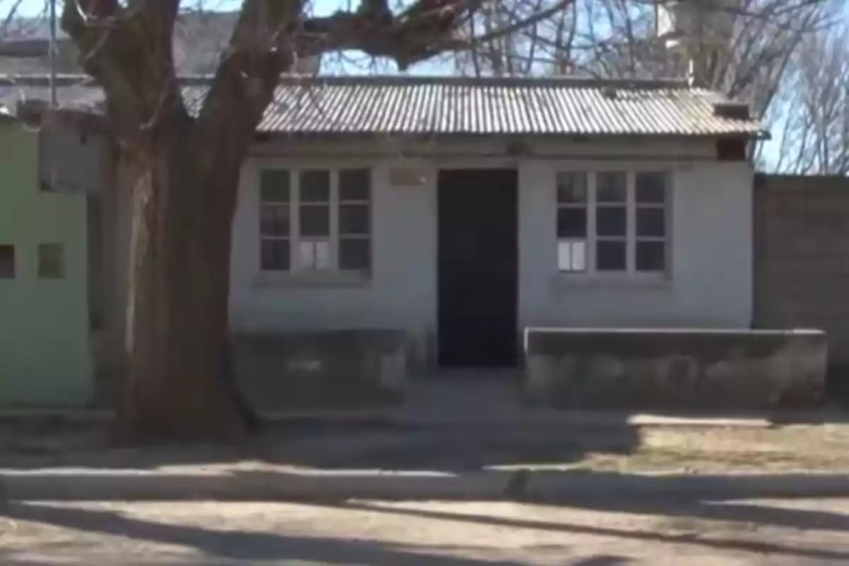 Fachada de una casa sencilla con techo de chapa, dos ventanas y un árbol grande al frente Fachada de una casa sencilla con techo de chapa, dos ventanas y un árbol grande al frente