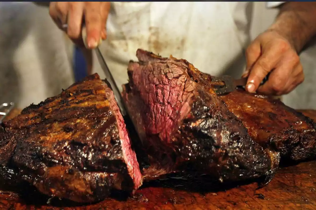 Persona cortando un gran trozo de carne asada jugosa sobre una tabla de madera