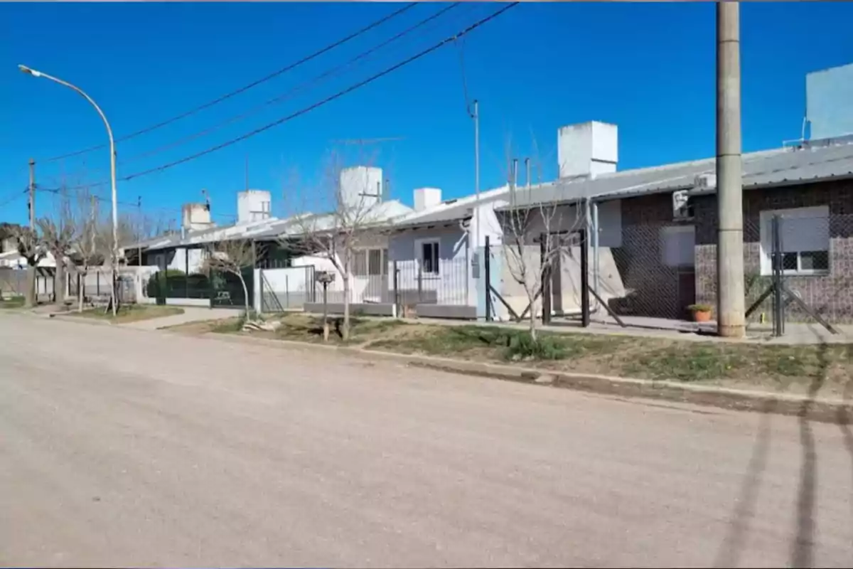Viviendas de una sola planta alineadas sobre una calle de tierra con árboles sin hojas y cielo despejado