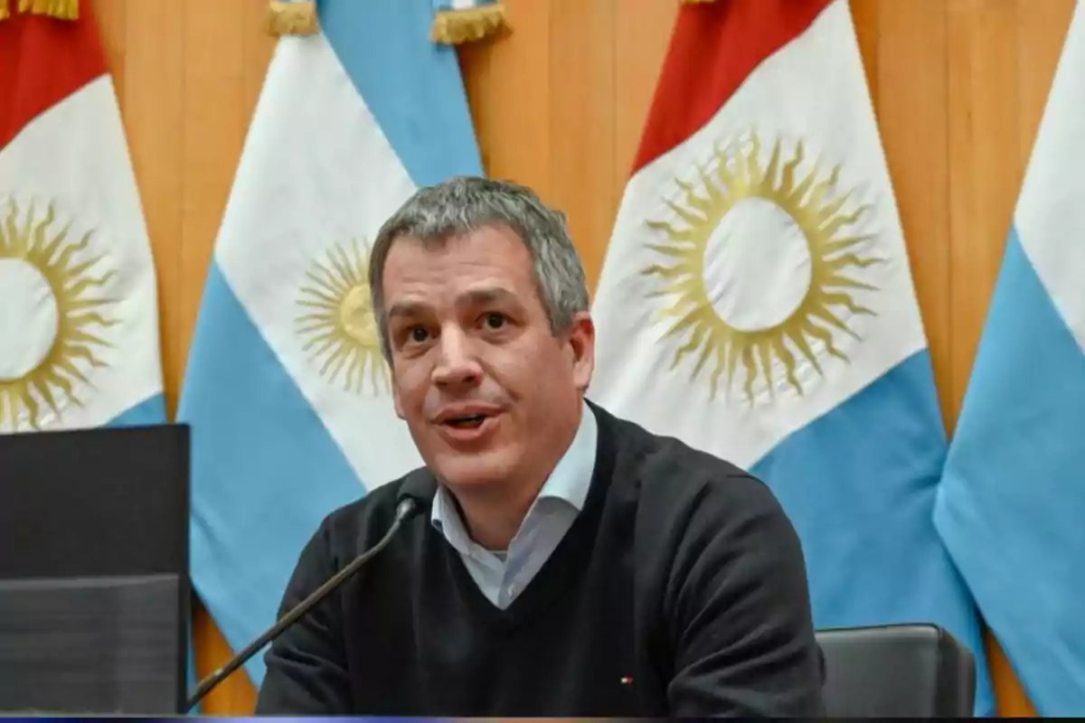 Hombre hablando en una conferencia con varias banderas de Argentina de fondo