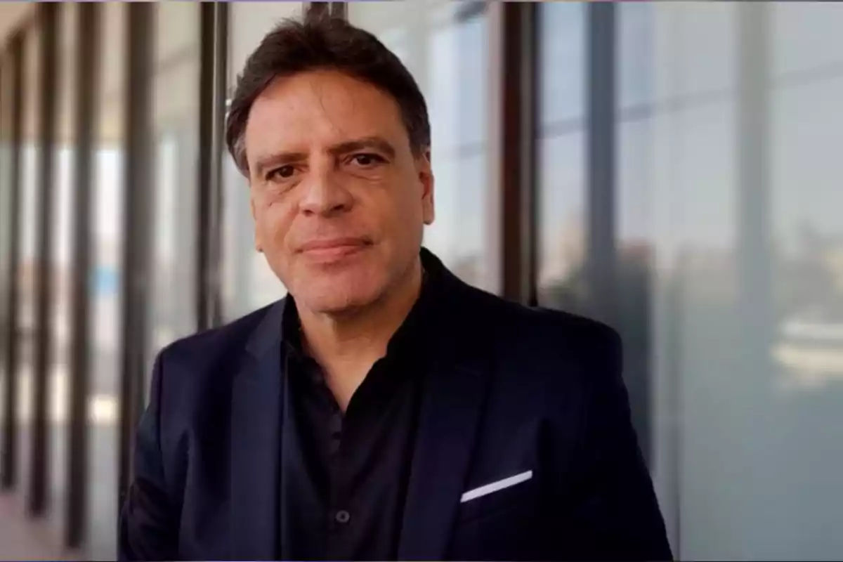 Dark-haired man wearing a black jacket posing in front of a glass wall Dark-haired man wearing a black jacket posing in front of a glass wall