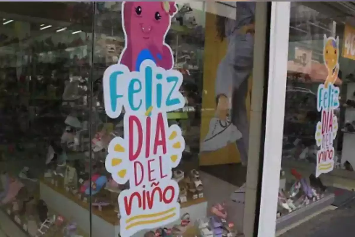 Escaparate de tienda de zapatos decorado con un cartel colorido que dice Feliz Día del Niño y un dibujo de un personaje rosa sonriente Escaparate de tienda de zapatos decorado con un cartel colorido que dice Feliz Día del Niño y un dibujo de un personaje rosa sonriente