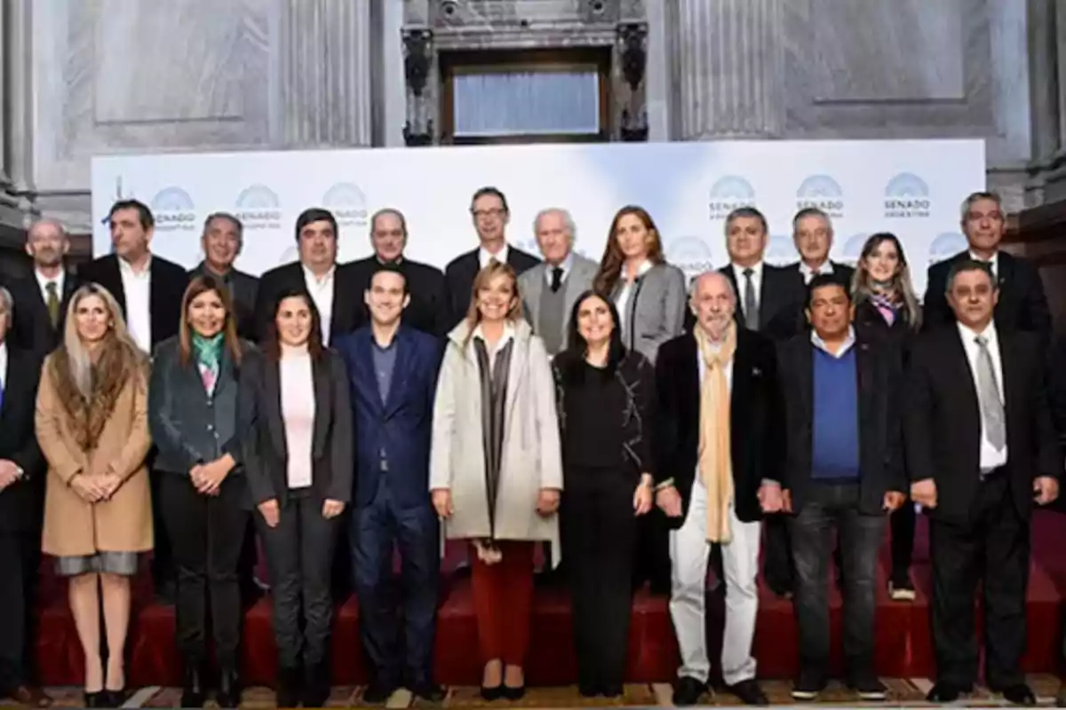 A group of people posing for a formal photo in an institutional building with a backdrop of Senate logos A group of people posing for a formal photo in an institutional building with a backdrop of Senate logos