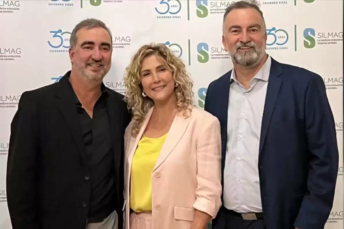 Three people pose smiling in front of a backdrop with logos of a company called Silmag. Three people pose smiling in front of a backdrop with logos of a company called Silmag.