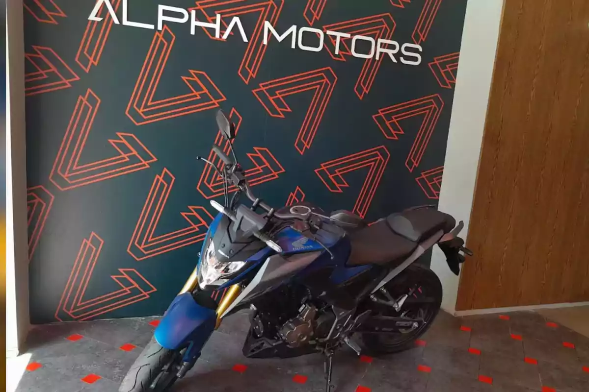 Blue motorcycle parked in a showroom with a decorative Alpha Motors background Blue motorcycle parked in a showroom with a decorative Alpha Motors background